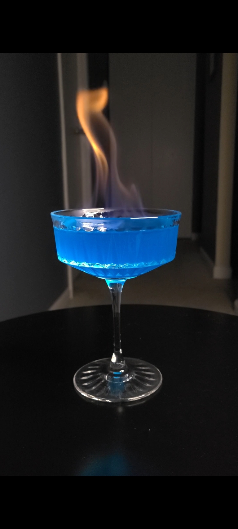 Flames Before Bed drink on black table. The drink is blue and is on fire.